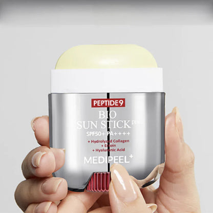 Hand holding a Medi Peel Peptide9 Bio Sun Stick against a gray background