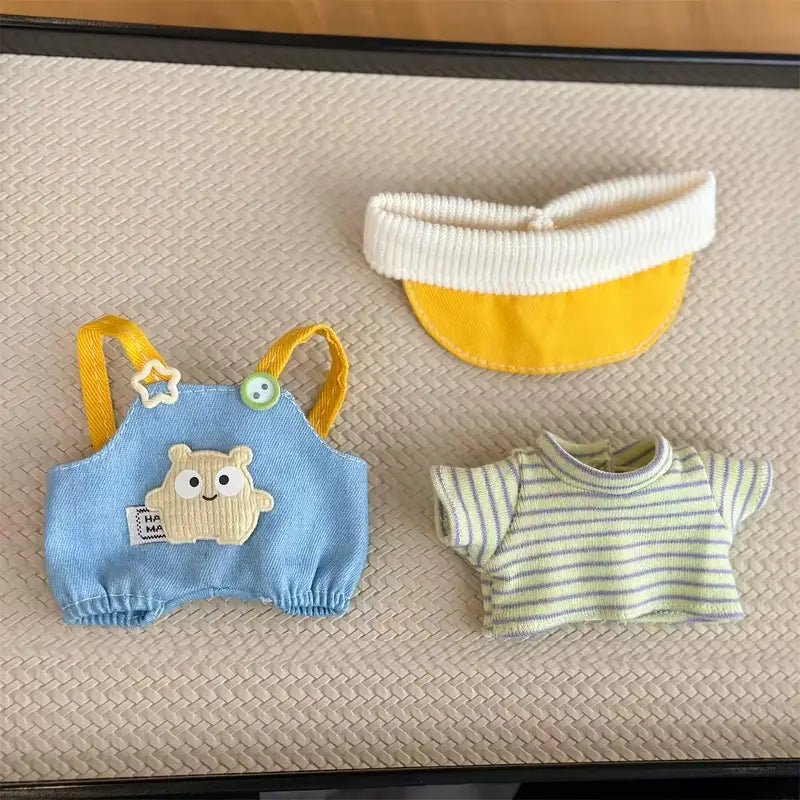 Set of baby clothing including a blue romper with bear design, yellow and white bib, and striped shirt on a textured surface.