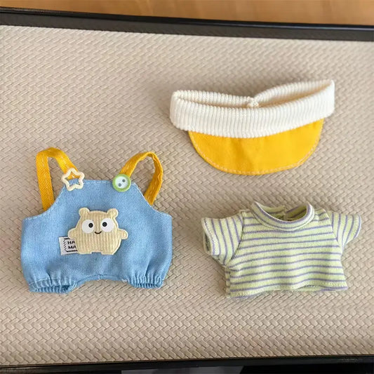 Set of baby clothing including a blue romper with bear design, yellow and white bib, and striped shirt on a textured surface.