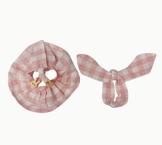 Flat lay of Zibuya’s two-piece Labubu outfit, including a pink gingham dress with bunny button straps and a matching tied bow headband, displayed on a white background.